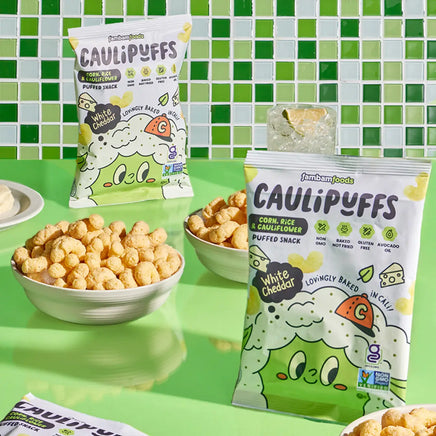 Bowls of CauliPuffs White Cheddar on a green table with a bag of puffs and a green tiled background