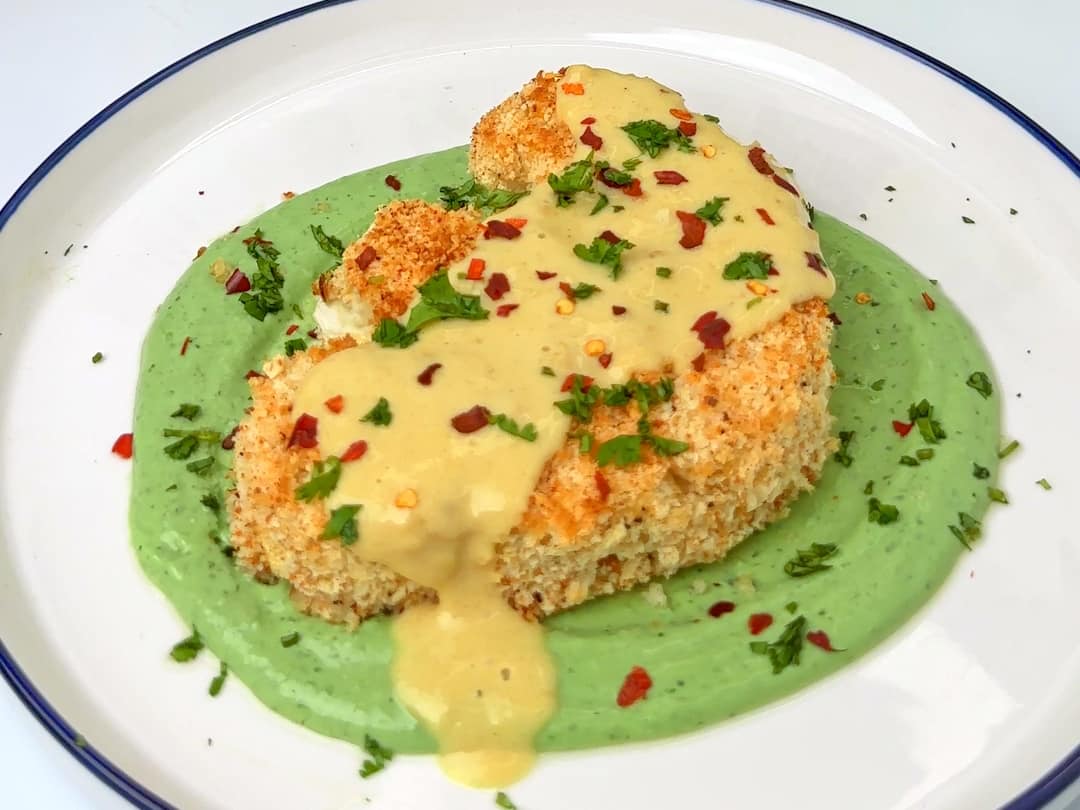 Cauliflower steak served on a plate with green sauce